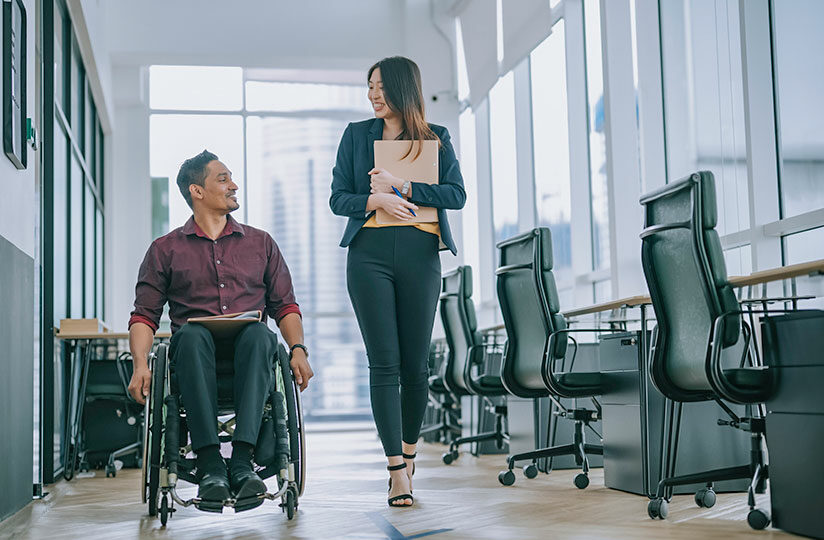 Mann im Rollstuhl neben laufender Frau in Büro