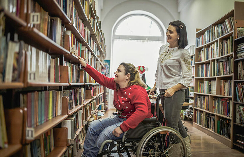 Frau in Rollstuhl und weitere Frau in Bibliothek