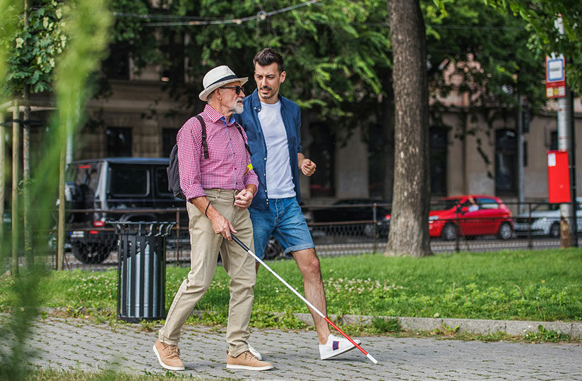 Mann mit Blindenstock und weiterer Mann durch Stadt laufend