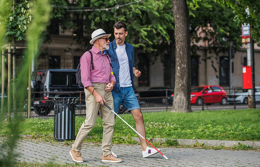 Mann mit Blindenstock und weiterer Mann durch Stadt laufend