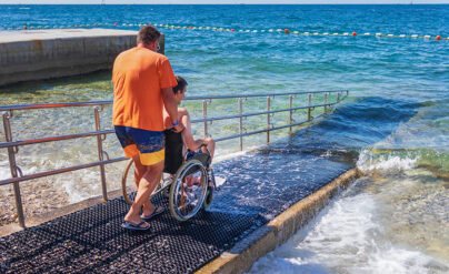 Mann schiebt weiteren Mann im Rollstuhl ins Meer