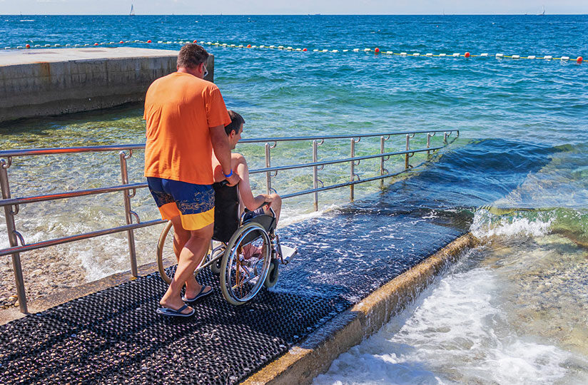 Mann schiebt weiteren Mann im Rollstuhl ins Meer